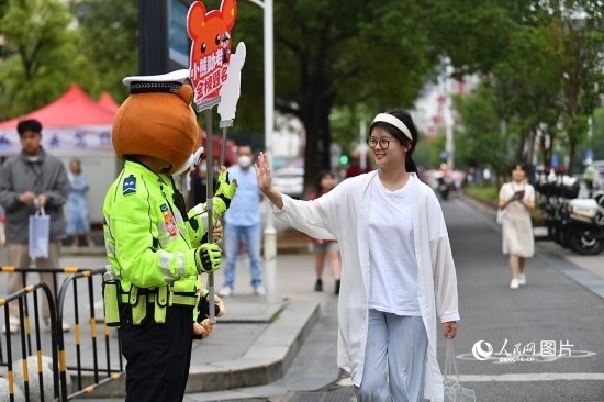 6月7日上午9時，隨著鈴聲的響起，2023年江西高考正式開考，江西省的53.57萬考生以縣（區(qū)）為單位隨機(jī)安排在全省256個考點、18968個考場參加高考。圖為“小熊交警”和考生擊掌鼓勵。 人民網(wǎng)記者 時雨攝