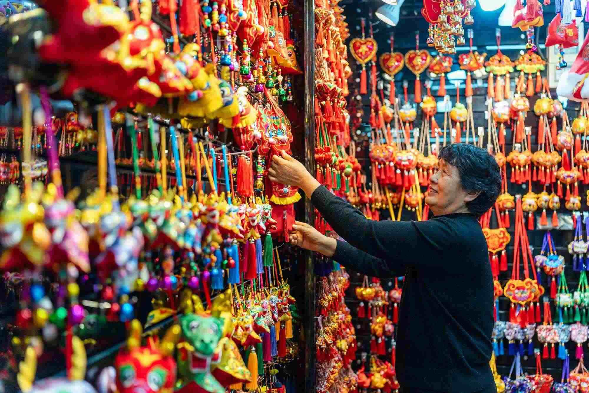 2023年12月11日，金華義烏國(guó)際商貿(mào)城，龍年喜慶用品掛滿攤位，顧客正在挑選中。