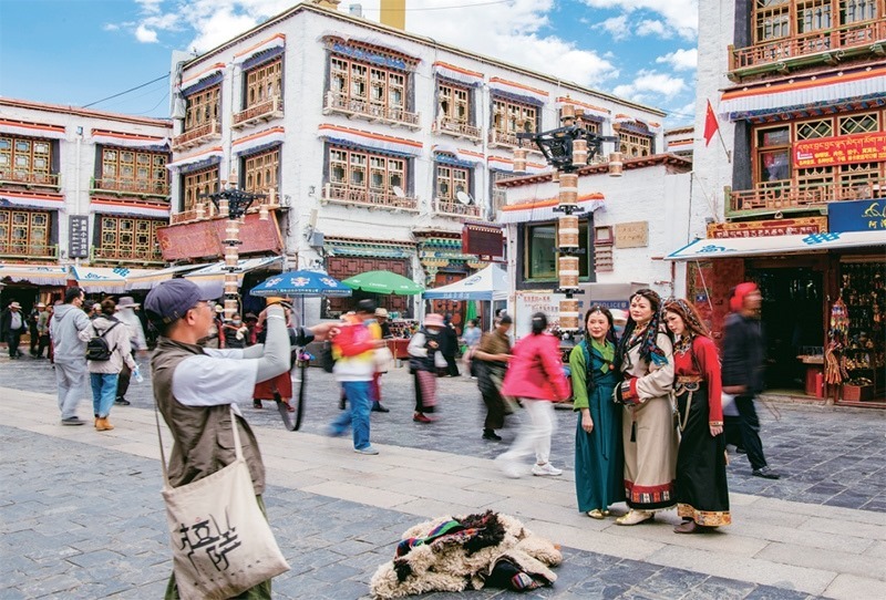 千年八廓街，見(jiàn)證民族團(tuán)結(jié)。2021年7月，習(xí)近平總書(shū)記來(lái)到位于西藏拉薩老城區(qū)的八廓街，感慨地說(shuō)：“千年八廓街，是我們各民族建起來(lái)的八廓街。各民族文化在這里交流交往交融，我們中華民族的大家庭在這里其樂(lè)融融?！眻D為2023年6月13日，游客身著藏裝在八廓街拍照留念。 新華社記者 姜帆/攝